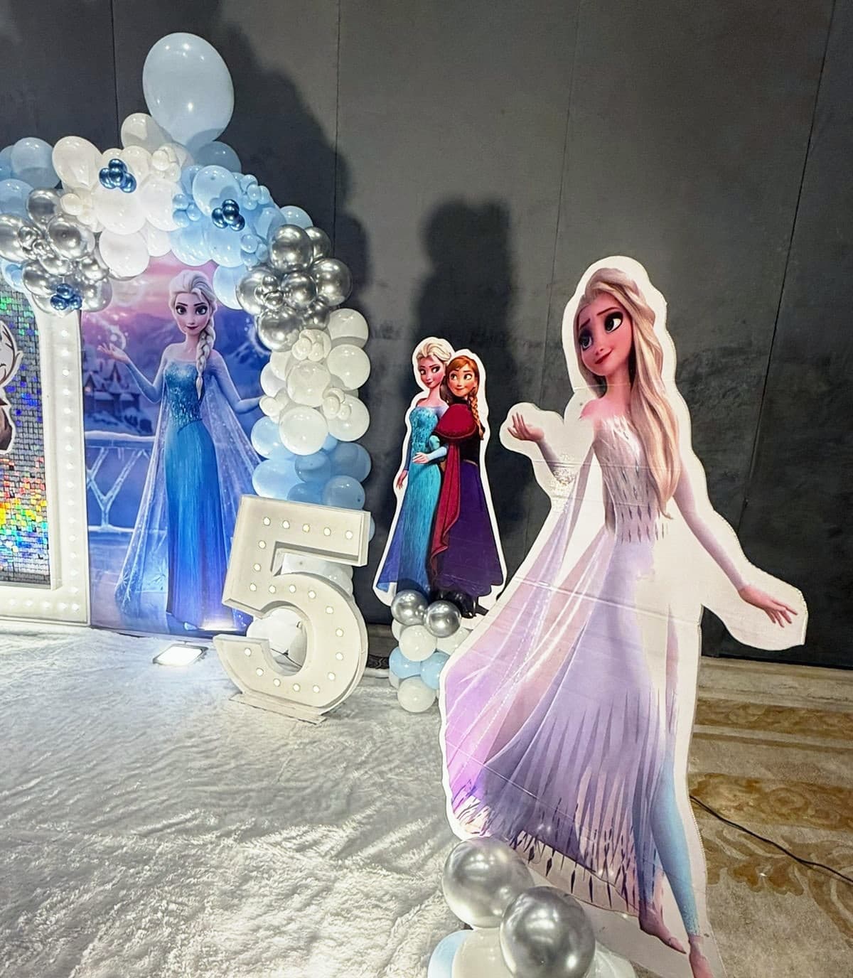 A Frozen stage with Elsa and Anna cut-outs and a lit number five